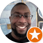 Headshot of a smiling Black man with glasses. A star icon is superimposed in the lower right corner.
