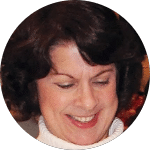 Smiling woman with short, curly brown hair wearing a white turtleneck. Her eyes are crinkled in laughter.