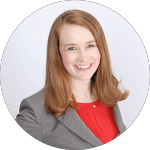 Smiling woman with red hair wearing a gray blazer and red blouse. Professional headshot for reviews, showcasing confidence and approachability.